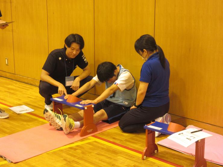 体育館で長座体前屈をする参加者をスタッフが計測している様子