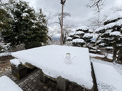 3cmほどの雪が積もったテーブルとベンチ。小さい雪だるまが乗っている。