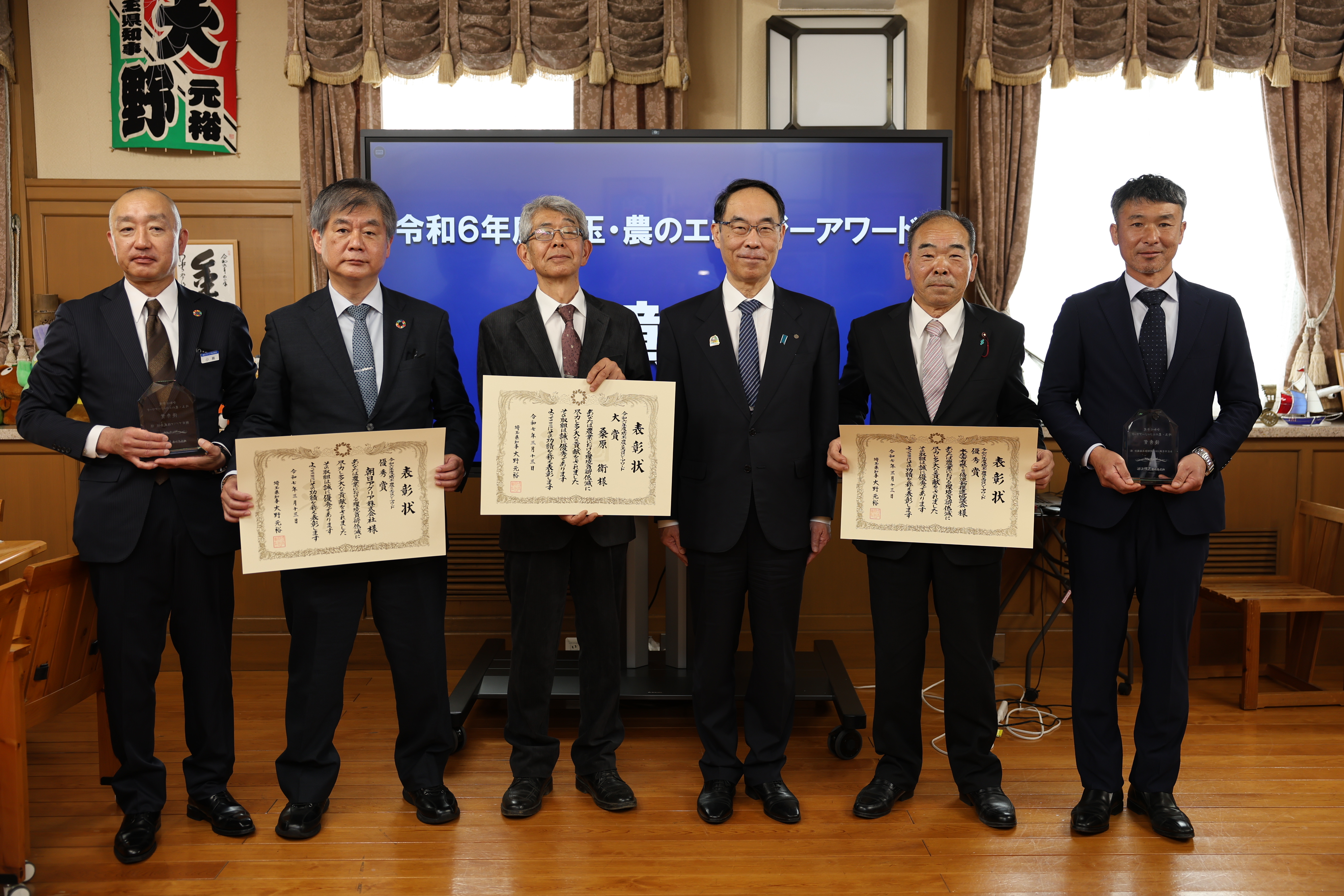 表彰式で訪問者らと記念写真を撮る知事の写真