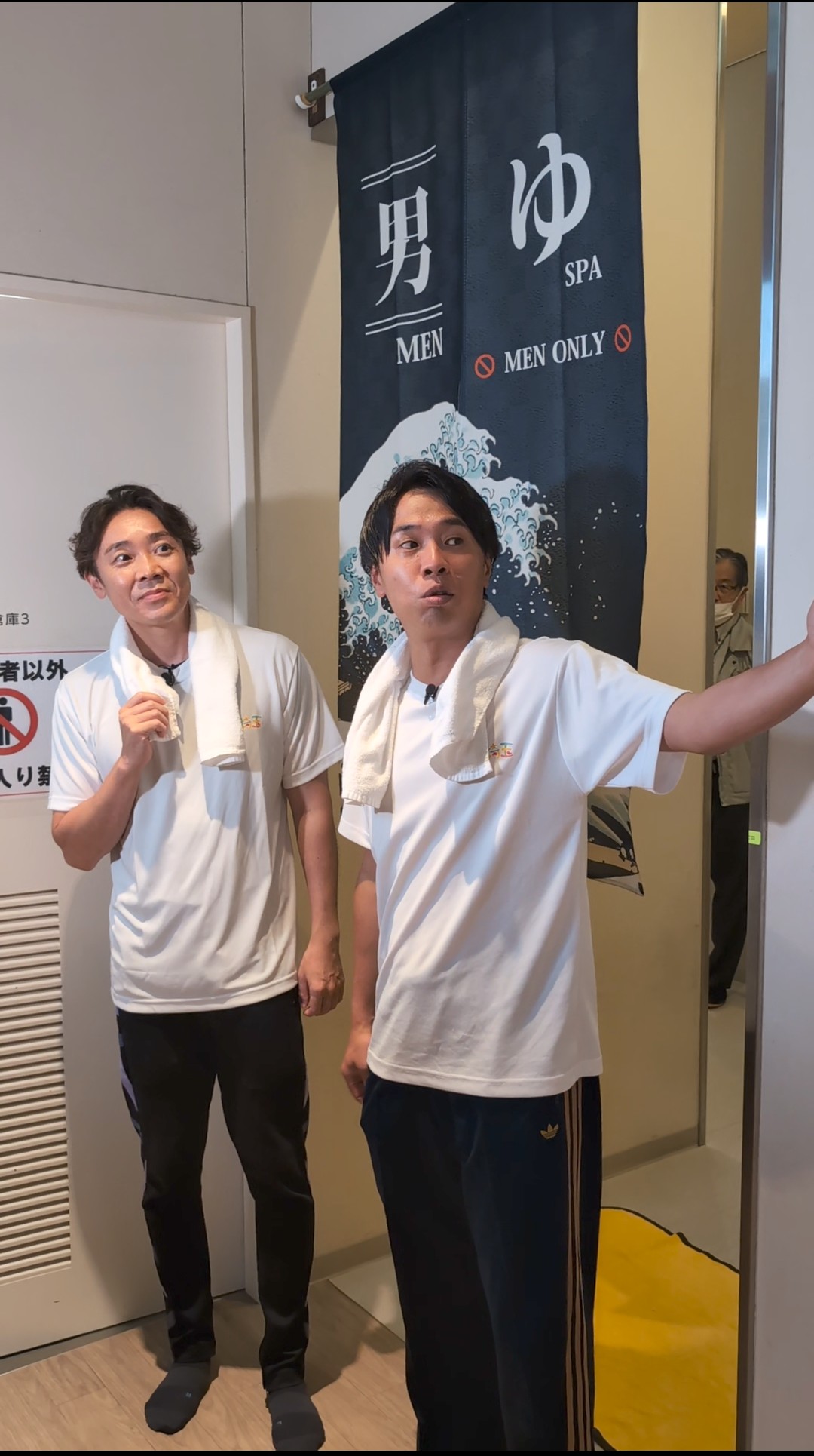 温浴施設でタオルを肩にかけているよしお兄さんとカナイ