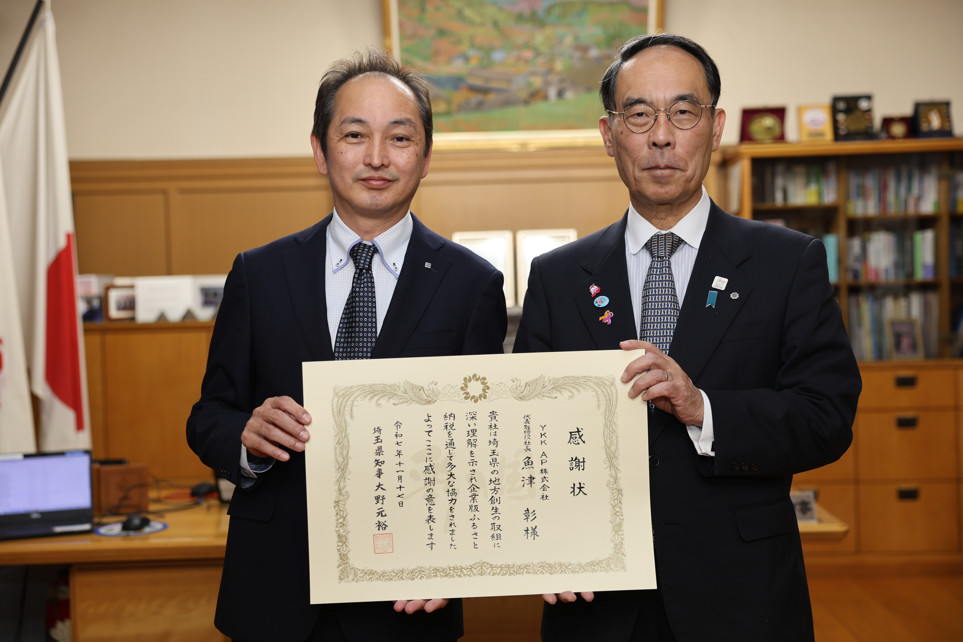 感謝状贈呈者と記念写真に映る知事の写真