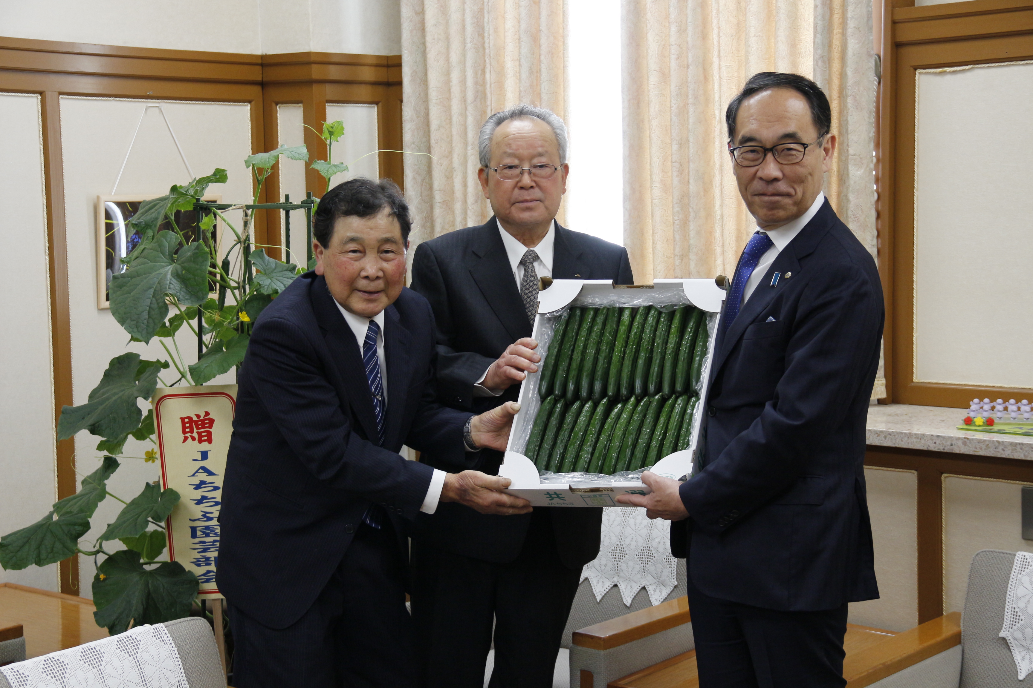 訪問者ときゅうりを持ちながら記念写真を撮る知事の写真